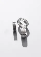 Anillo de acero quirúrgico plateado con diseño labrado de guarda griega en color negro.