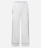 Conjunto de pijama de dos piezas, color blanco, compuesto por una blusa de manga larga con escote en V ribeteado en negro y un pantalón recto con ribetes negros en los bordes.