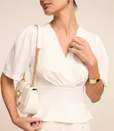 Blusa blanca de crepé con escote en V sobrepuesto, mangas cortas y recorte en la cintura con aspecto de volado.