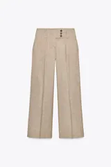 Pantalón de tiro alto color beige, con bolsillos delanteros y falsos bolsillos traseros. Pierna ancha y cierre frontal con ganchos metálicos y botones.