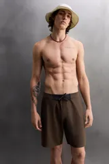 Bañador corto color marrón con cintura elástica negra ajustable con cordón. Tiene un bolsillo lateral con cierre de cremallera y costuras planas termofijadas.