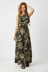 Vestido largo sin mangas, con estampado floral en tonos negro y beige/dorado. Presenta cuello bote, recortes laterales en la cintura y borlas colgantes en los laterales superiores. La falda es recta y fluida.