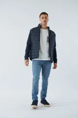 Campera negra con cuerpo acolchado de nylon y mangas de felpa. Tiene cuello alto, cierre frontal, bolsillos laterales con cierre, logo estampado en el pecho y logo de goma en la manga.