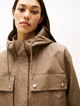 Campera marrón de Tommy Hilfiger con capucha con cordón ajustable, cierre de cremallera oculto con botones a presión, dos bolsillos delanteros tipo sobre con botón, logo metálico en el puño y corte amplio.