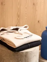 Canguro color crema con capucha, cordones ajustables, bolsillo tipo canguro y puños y bajo acanalados. Estampado con texto en el pecho.