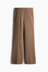 Pantalón de vestir color marrón claro, de tiro alto y corte bootcut. Presenta bolsillos laterales y traseros ribeteados, cierre frontal con botón y pliegues delanteros y traseros.