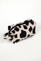 Neceser rectangular de tela con estampado de vaca en blanco y negro, cierre superior con cremallera negra y asa lateral.