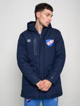 Parka blanca con capucha, cierre frontal con cremallera y botones a presión, cuatro bolsillos frontales con solapa y puños ajustables. Incluye logo de Umbro y escudo del Club Nacional de Football en el pecho.