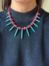 Collar corto con cuentas de cerámica rojas, pinchos turquesa de piedra reconstituida, cristales checos y mostacillas. Se cierra con cadena de acero quirúrgico para regular el largo.