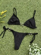 Conjunto de bikini negro con corpiño triangular con argolla metálica y bombacha colaless con tiras para atar y argollas en los costados.