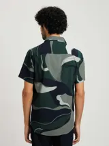 Camisa blanca de manga corta con estampado de hojas en negro y gris, cuello clásico y corte recto.