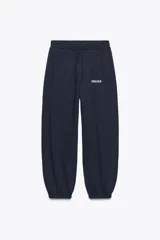 Pantalón jogger azul marino de tiro alto con cintura elástica ajustable, bolsillos delanteros, texto blanco estampado en la pierna izquierda y puños elásticos en los tobillos.