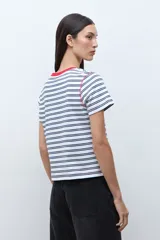Remera de manga corta con rayas horizontales blancas y azul marino. Presenta cuello redondo con ribete rojo y costuras expuestas en rojo en los hombros.