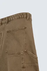 Bermuda color verde militar, de corte relaxed fit, con bolsillos frontales y traseros tipo plaqué, detalle de tira y bolsillo multifunción en la pierna, y bajo irregular.