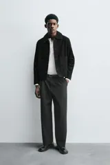 Cazadora de corte cropped fit, confeccionada en piel con acabado serraje (gamuza) de color negro. Presenta cuello solapa, manga larga, dos bolsillos de plastrón en la cadera y cierre frontal de botonadura.