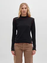 Polera negra de tela rib con cuello alto y mangas largas. Presenta pespuntes rojos en cuello, hombros y puños.