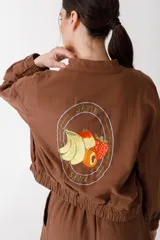 Bomber color coral confeccionada en mezcla de algodón y lino, con cierre frontal y puños elásticos. Presenta un bordado grande en la espalda inspirado en la colección La Verdulería.