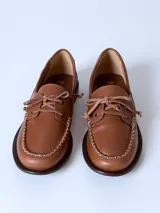 Mocasín de cuero color marrón claro, con cordones y detalle de costuras en la puntera.