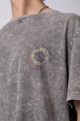 Remera de hombre color gris oscuro con efecto gastado (snow wash), corte semi-oversize y un pequeño estampado circular en el pecho que simula una obra de arte.