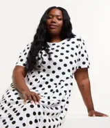 Vestido midi blanco con lunares negros, de corte suelto, cuello redondo y mangas cortas.