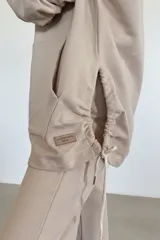 Canguro beige oversize de tejido suave con capucha, cordones ajustables y bolsillo tipo canguro.