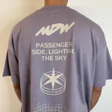 Remera lila con estampado en la espalda que incluye texto, un logo y un diseño geométrico.