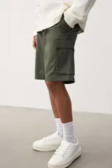 Short cargo color verde militar, de corte regular, con cintura elástica ajustable con cordón, bolsillos laterales, bolsillos cargo con solapa y cierre autoadherente en las piernas y bolsillos traseros con solapa y cierre autoadherente.