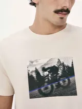 Camiseta blanca de algodón con cuello redondo y mangas cortas. Estampa rectangular con borde negro que contiene la frase "NATURAL ATMOSPHERE" en letras mayúsculas y una imagen de montañas y mar.