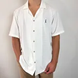 Camisa de manga corta en tejido de punto con textura, color blanco. Posee un calce oversize, cuello con solapa, cierre frontal de botones y un pequeño logo bordado en el pecho.