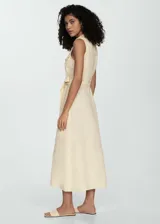 Vestido midi color amarillo pálido de lino, sin mangas, con cuello camisero, corte recto, cinturón decorativo y cierre frontal con botones.