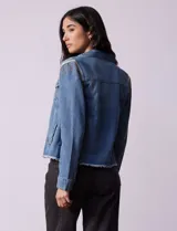 Campera de jean celeste de la marca Baccini, con cierre central, bolsillos delanteros, apliques colgantes de tachas en los hombros y terminación desflecada en el ruedo.