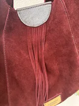 Cartera tipo hobo de gamuza color borgoña con flecos y asa corta de cuero marrón.