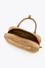Bolso mini bowling color camel de serraje, con doble asa de mano y correa bandolera extraíble. Tiene un bolsillo interior con cremallera y cierre principal con cremallera y tirador.