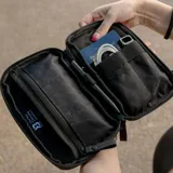 Riñonera negra con correa ajustable, confeccionada en material impermeable xPac X21. Cuenta con 7 bolsillos internos y 2 externos, organizador con apertura de 180°, espacio para cables y cargadores, detalles en color ladrillo y cierres impermeables.