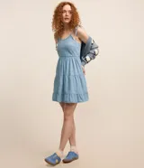 Vestido corto de jeans celeste, con breteles finos con lazos, escote en U, espalda descubierta y falda de tres niveles con volados.
