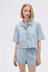 Camisa celeste de jean, corte cropped, con cuello camisero, cierre frontal con botones y mangas cortas.