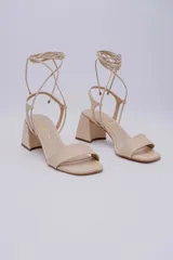 Sandalias de tacón color beige, con punta cuadrada, tira ancha sobre los dedos y tiras finas que se atan al tobillo.