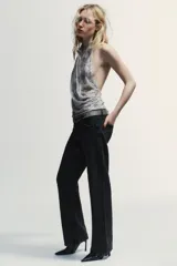 Top halter de tul color gris claro, con escote fluido drapeado y espalda descubierta. Presenta bordados con aplicación de abalorios en tonos oscuros y dorados.