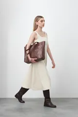 Cartera tipo tote bag en símil cuero color marrón oscuro, con bordados decorativos en blanco que evocan un estilo western. Cuenta con asas largas para llevar al hombro.