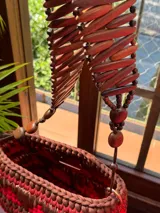 Bolso de mano tejido a mano con tiras de material orgánico en tonos tierra (rojo, marrón, beige) sobre una base de eco-cuero. Posee un asa de mano hecha de un cinturón vintage.