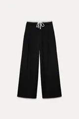 Pantalón negro de tiro alto con doble cintura elástica ajustable con cordón, pinzas frontales, bolsillos delanteros y falso bolsillo de vivo en espalda.