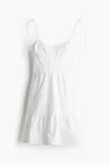 Vestido corto blanco de popelina de algodón, con breteles finos que se atan en moño, escote corazón y falda acampanada con volado en el ruedo.