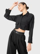Blusa negra corta de manga larga con cuello camisero, cierre frontal con botones y dos bolsillos con fuelle en el pecho.