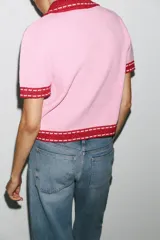 Chaqueta color blanco de punto con cuello solapa y manga corta. Tiene cierre frontal con botones color naranja y ribete en azul marino y naranja.