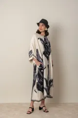 Vestido largo color natural con estampado de hojas de palmera en tonos verdes. Tiene corte amplio tipo túnica, cuello redondo, mangas tres cuartos, bolsillos laterales y ruedo con ribete.