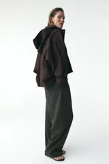 Trench corto color negro, con cuello solapa y capucha desmontable mediante botones. Manga larga tipo murciélago acabada en trabilla ajustable. Bolsillos laterales. Forro interior combinado. Cierre frontal con botones. Tejido repelente al agua.