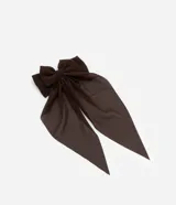 Accesorio para el pelo color marrón oscuro, con forma de lazo y caida de tejido. Modelo pinza.