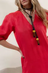 Vestido largo rojo con escote en V, mangas abullonadas con elástico en el puño y detalle de pespunte en contraste. Presenta un canesú con efecto punto smock y bolsillos laterales.