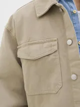 Campera de denim color beige, con cuello amplio, puños con botones y cierre frontal con botones. Incluye bolsillos en el pecho y laterales. Tejido denim de sarga resistente y con protección contra el viento.