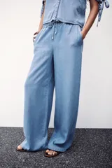 Pantalón celeste de tiro alto con cintura elástica ajustable con cordones, bolsillos delanteros y traseros, y pernera ancha.